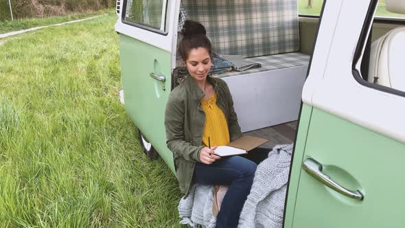Woman sitting in camper and writing in daybook