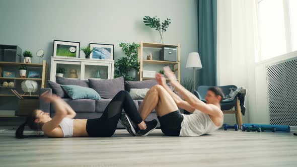 Young Couple Doing Sports Together at Home Exercising Abd and Clapping Hands alt