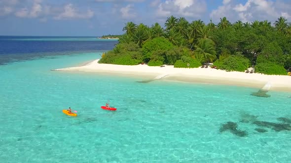 Aerial drone view of a man and woman couple kayaking around a tropical island alt