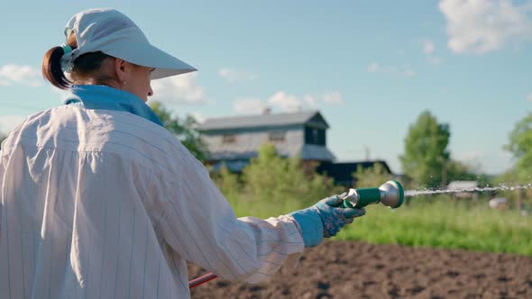 Woman Holding a Water Hose and Watering Beds or Plants in the Backyard alt