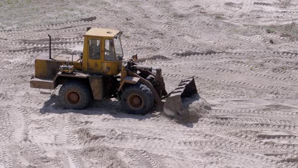 Old Tractor on Rubber Wheels Moves Sand Using a Bucket on Construction Site alt