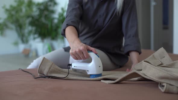 Woman Uses a Machine for Removing Pellet and Spools From Clothes and Fabric on Black Trousers