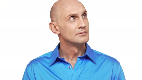 Middleaged Caucasian Bold Male in Blue Shirt Standing on White Background Being Deep in Thoughts alt