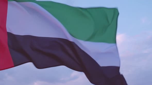 Close-up of the flag of the United Arab Emirates waving in the wind against a cloudless blue sky. alt