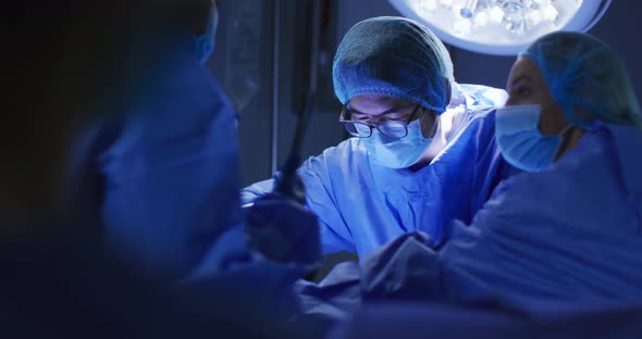 Diverse surgeons wearing face masks and protective clothing in operating theatre alt