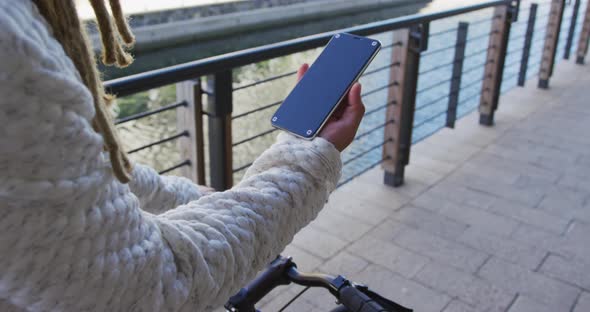 Mixed race man with dreadlocks riding a bicycle in the street using smartphone alt