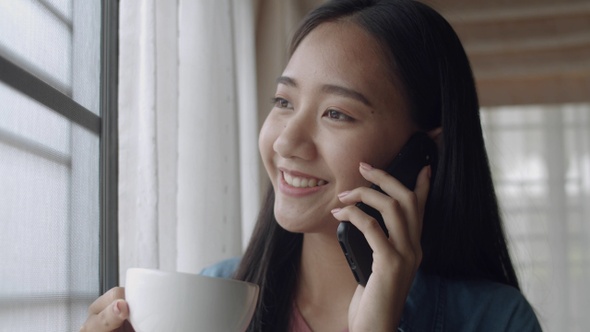 Smiling young Asian woman drinking coffee and talking on Phone.