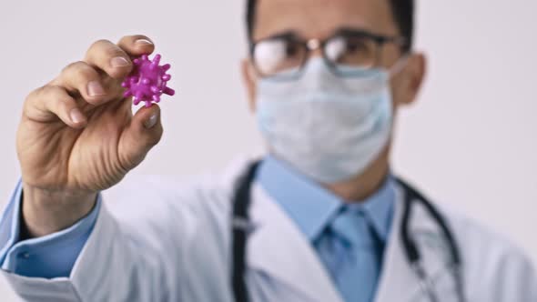 Male Handsome Doctor in Protective Mask and Glasses Shows Covid-19 Virus Cell alt
