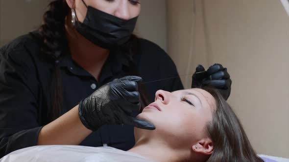 A microblading master is measuring woman's eyebrows. Lady is lying at studio.