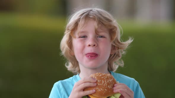 Blond boy eats delicious fresh hamburger