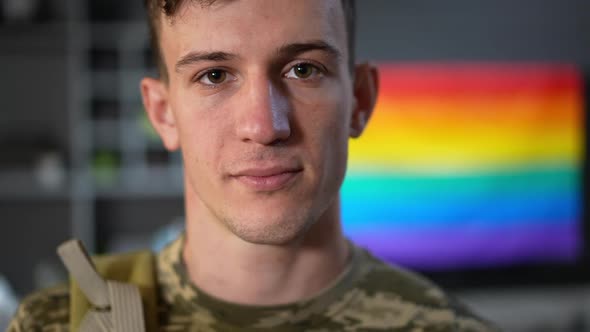 Headshot Portrait of Gay Soldier Posing Indoors with Rainbow Flag at Background alt