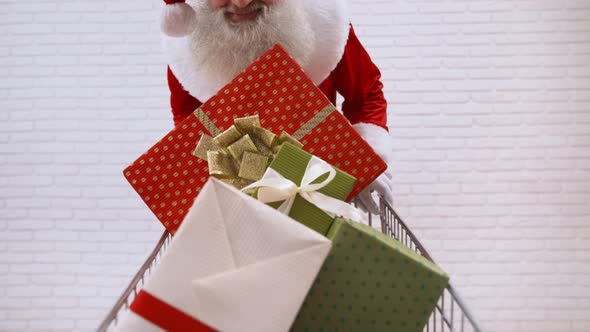 Senior Santa Claus Pushing Shopping Cart Full of Gift Boxes alt