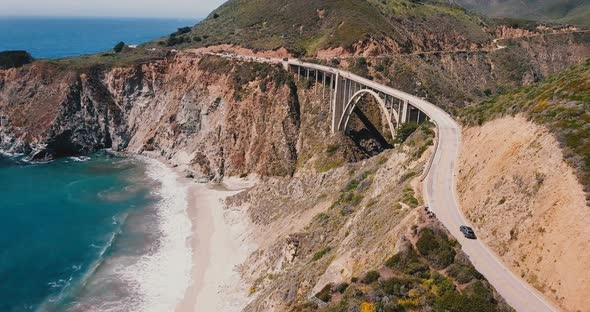 Amazing Static Aerial Shot of Car Moving Through Epic Bixby Creek Bridge on Highway alt