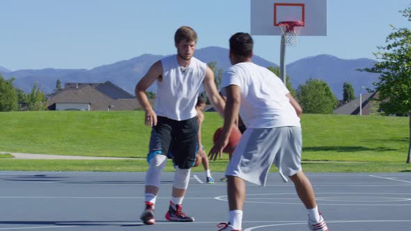 Friends playing basketball at park, one on one