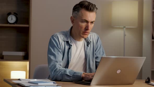 Serious focused determined young businessman or freelancer in casual clothes sitting at kitchen alt