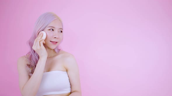 Asian young woman standing and wearing her makeup with pink background alt