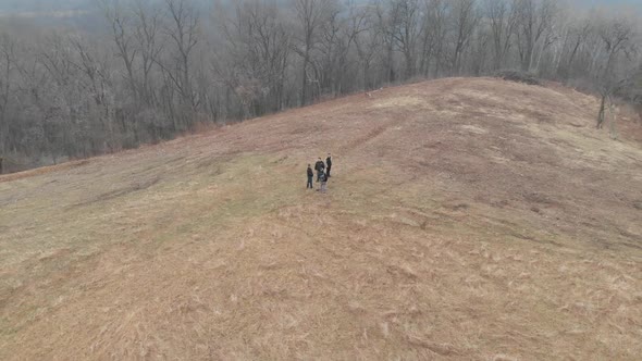aerial footage spinning in circle of people on a dry pastureland, trees around alt