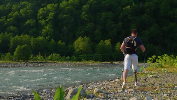 Male Traveller with Disabilities is Walking Alone Over Mountain River Shore alt