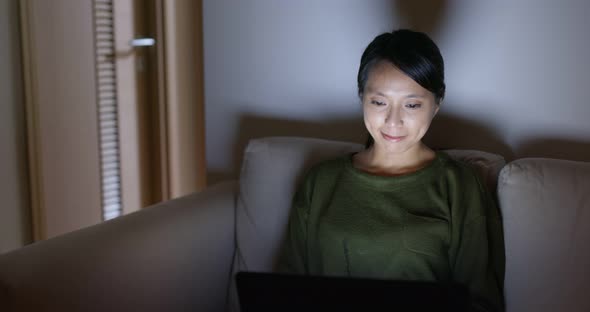 Woman sit on sofa and work on computer at night