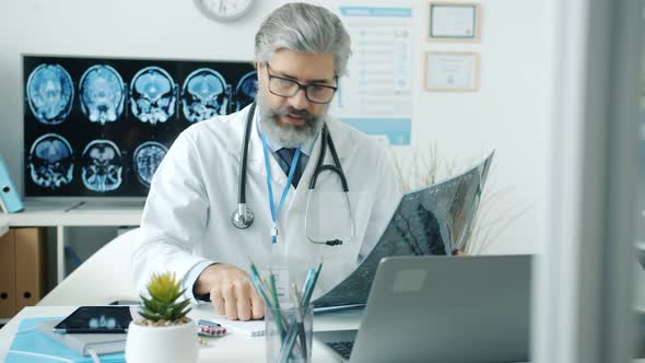 Experienced Doctor Studying MRI Image and Using Computer Typing Working in Hospital alt