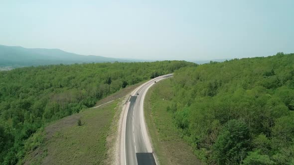 Aerial View of an Asphalt Intercity Country Road Between Green Forest with Vehicles Driving on It alt