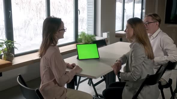 Three aspiring entrepreneurs are discussing a project with a green mockup screen on a tablet alt