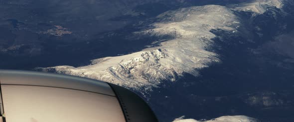 The plane flies over the snowy mountain peaks. View through an airplane window alt