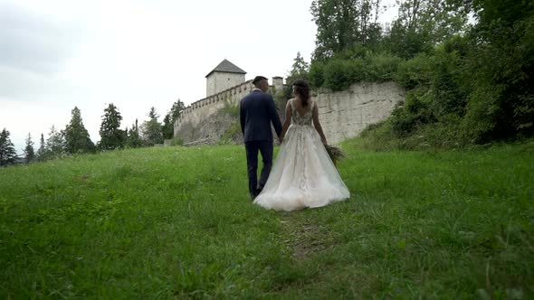 Newlyweds groom and bride walk on green meadow near old medieval castle Salzburg Austria