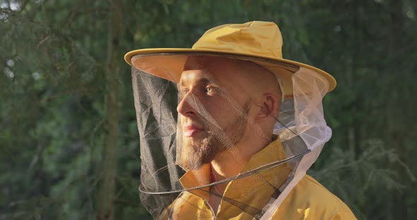 Smiling Male Beekeeper in the Forest in the Morning with the Rising Sun Wearing a Yellow Overalls alt