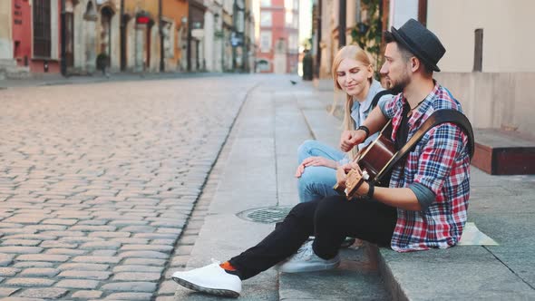 Mman and Woman Sitting on Sidewalk, Playing Guitar and Having Rest alt
