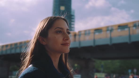 Young woman looks around with moving subway in the back alt