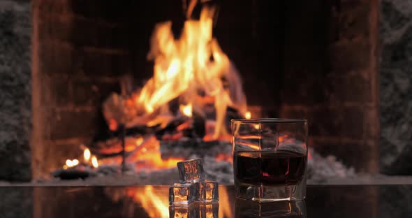 Glass with Whiskey or Cognac on the Background of Fire in the Fireplace alt