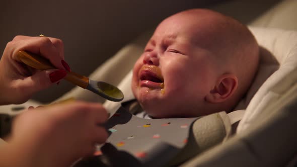 Mother Giving Food to Baby Boy Puree From Spoon in Highchair at Home