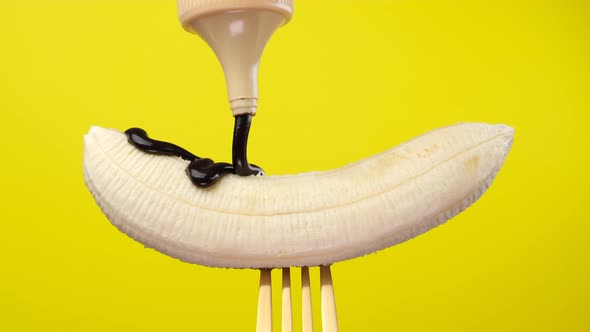 pour chocolate syrup on raw banana close up on yellow background  alt