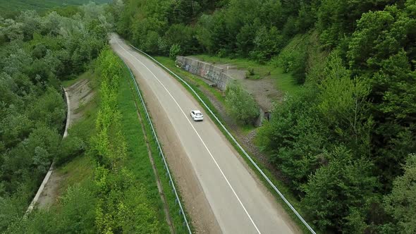 Aerial Top Down  View of White Car Driving on Rural Road in Forest alt