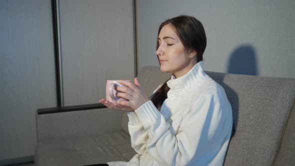 Pretty Girl Reading a Book and Drinking Coffee on the Sofa at Home alt