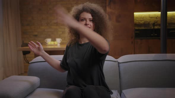 Young Curly Woman Waving Hands Trying To Catch Annoying Fly in Front of Her Face Sitting on Couch at