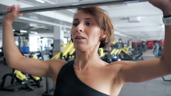 Woman is Doing Set of Reps Exercise with Barbell Lifting It Over the Head in Gym