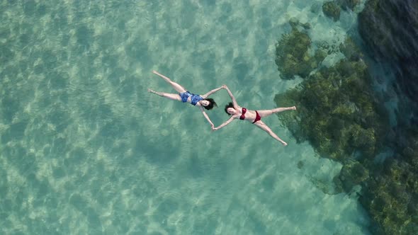 Two Beautiful young woman swimming, lying on a water surface in crystal clear ocean