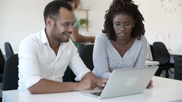 Smiling Colleagues Talking and Reading Information From Laptop alt