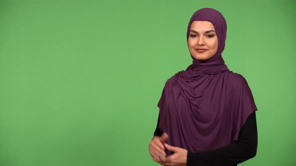 A Young Beautiful Muslim Woman Presents Something to the Camera with a Smile  Green Screen