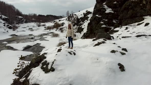 A Tourist Girl in a Jacket Stands on the Slope of a Snowy Mountain in Nature