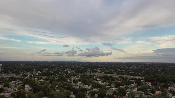 An aerial view of a quiet suburban neighborhood on Long Island. It is a cloudy day. The sky is beaut alt