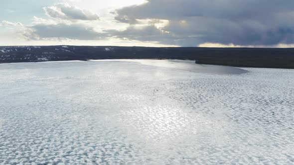 Drone Flying Above Frozen Lake with Melting Ice Shield and Clouds Reflection alt