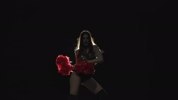 Energetic Dance of Cheering Performed By a Cute Cheerleader Holding Pompoms Against Backlit Black alt
