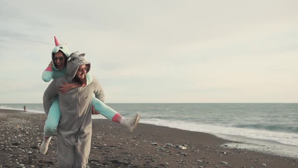 Happy Spouses in Kigurumi Costumes Running on a Stone Beach Near the Sea alt