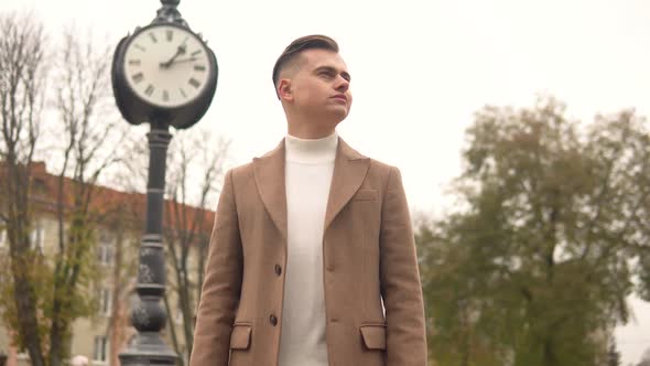 Portrait of a Handsome Fashionable Man in Brown Coat Against the Background of Street Clocks. New alt