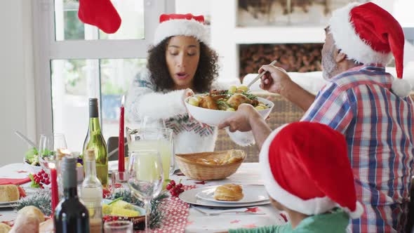 Happy african american multi generation family wearing santa hats and celebrating in kitchen alt