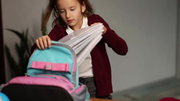 Schoolgirl put books and notes into backpack at home,