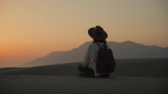 Young woman sitting on the sand and looking at the sea alt
